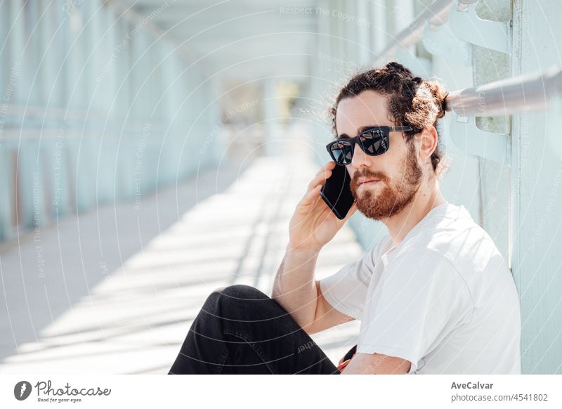 Junge Hipster-Mann auf dem Flughafen oder Busbahnhof warten, während ruft jemand mit dem Telefon, Gepäck, Taschen und Koffer. Junger Mann lange Haare Hipster Reisende mit Sonnenbrille, Kopie Raum, sonnigen Tag