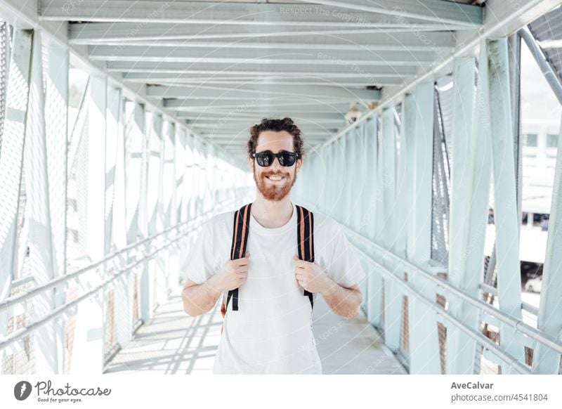 Porträt eines jungen Mannes auf dem Flughafen oder Busbahnhof, Gepäck, Taschen und Koffer. Lächelnder Hipster-Reisender mit Sonnenbrille, Kopierraum, sonniger Tag