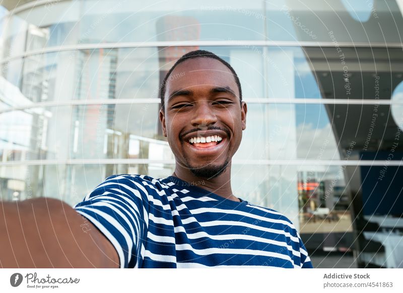 Fröhlicher schwarzer Mann macht Selfie auf der Straße Selbstportrait Großstadt Gebäude einfangen Fotografie Gedächtnis modern Afroamerikaner Hobby männlich