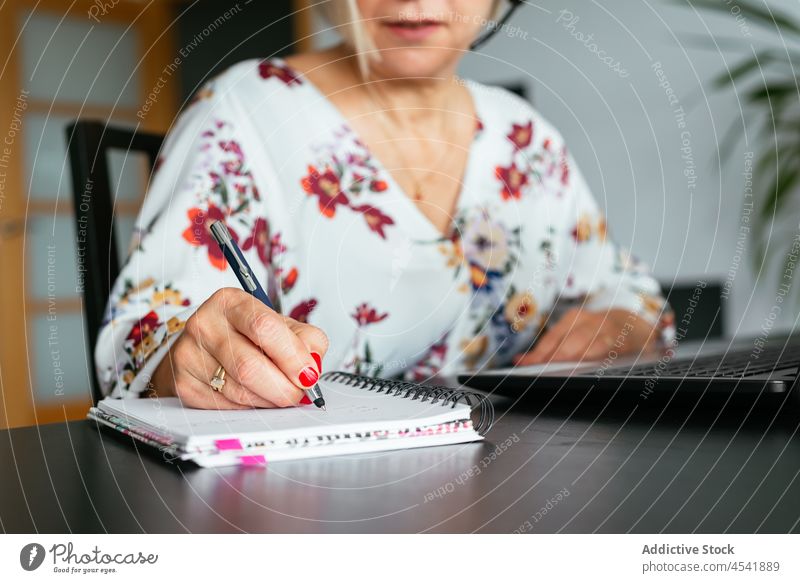 Anonyme reife Frau schreibt in ein Notizbuch, während sie an einem Laptop arbeitet schreiben Notebook Arbeit benutzend Konzentration beschäftigt abgelegen Job