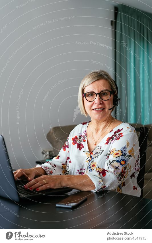 Ernste reife Frau mit Brille und Headset tippt auf einem Laptop Telearbeit Betreiber benutzend Tippen online Internet Arbeit Apparatur beschäftigt Entfernung
