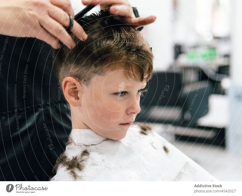 Friseurin schneidet die Haare eines Jungen im Salon Klient Stylist Haarschnitt geschnitten Schere positiv Prozess Verfahren Arbeit Frisur Kap Schürze Kind