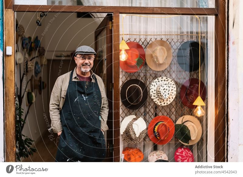 Älterer männlicher Besitzer steht in der Nähe des Eingangs eines modischen Hutgeschäfts Mann Werkstatt Vitrine Meister handgefertigt Sammlung Kleinunternehmen