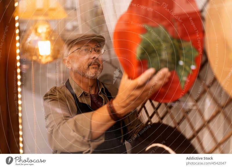 Bärtiger männlicher Kunsthandwerker, der hinter einer Vitrine Hüte aufhängt Mann hängen Hut Merchandise Basteln kreativ Kunstgewerbler Stil Kleinunternehmen