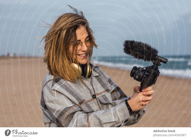 Junge Frau am Meeresufer und Videoaufnahme mit Kamera Strand vlog Aufzeichnen heiter Blogger Fotoapparat Urlaub Glück MEER Sand jung tausendjährig trendy