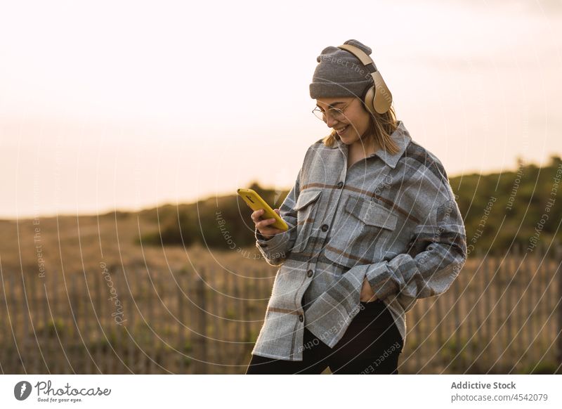 Glückliche junge Frau, die ein Smartphone benutzt und mit Kopfhörern in der Natur Musik hört zuhören Lächeln Landschaft Wiedergabeliste meloman Nachricht