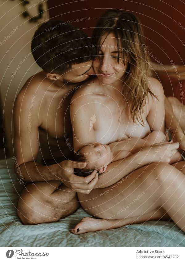 Glückliches nacktes Paar mit Baby kuschelnd auf dem Bett Familie neugeboren Kuss stillen Liebe Zusammensein Umarmen Partnerschaft schließen Ehefrau Ehemann