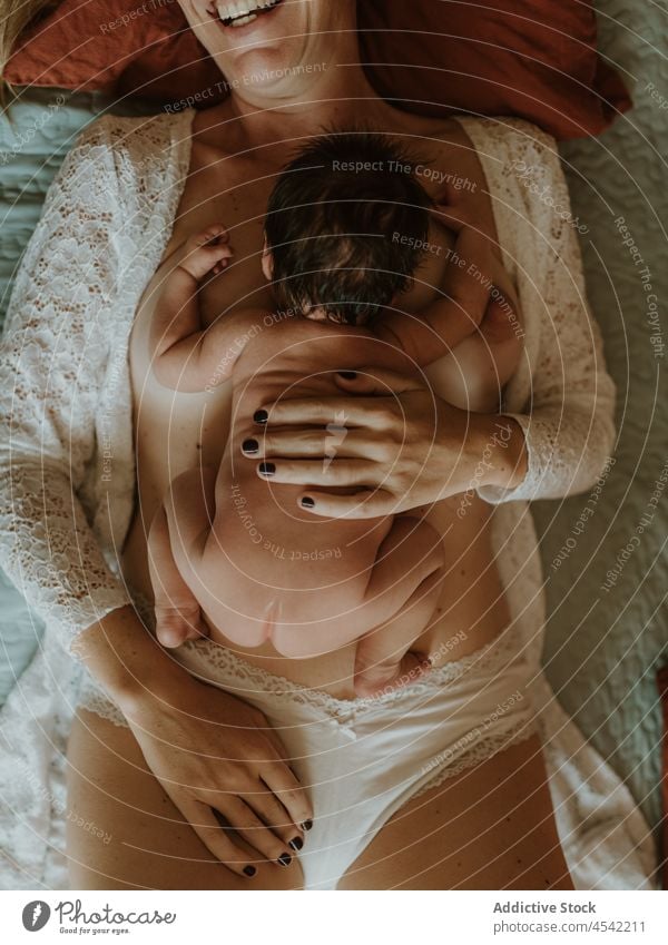 Crop glückliche Mutter mit Neugeborenem auf dem Bett liegend nach dem Stillen Frau Baby Lügen Lächeln heiter stillen Zusammensein Umarmen Glück nackt neugeboren