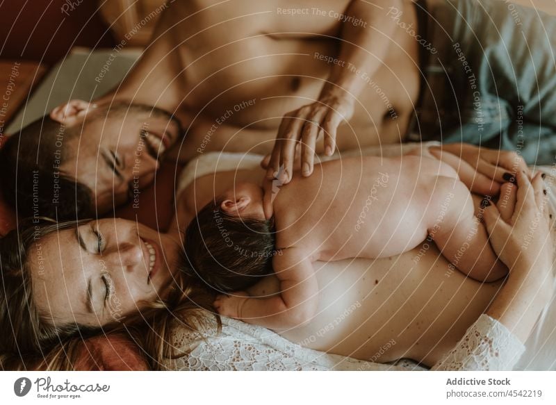 Glückliches nacktes Paar mit Baby kuschelnd auf dem Bett Familie neugeboren stillen Liebe Zusammensein Umarmen liegend Partnerschaft Ehefrau Ehemann Pflege