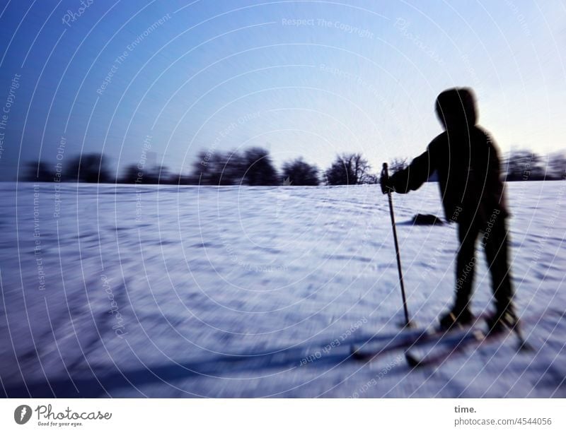 Raumgleiterin • Vermummtes Mädchen mit Skiern auf verschneiter Wiese im Abendlicht ski skisport wintersport schnee wiese abendlicht horizont anorak kapuze