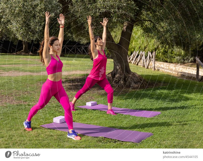 Zwei barfuß lebende Frauen, die im Sommer im Park Yoga oder Dehnübungen machen Pilates Asana Gesundheit strecken rosa grün sonnig mittleres Alter jung im Freien