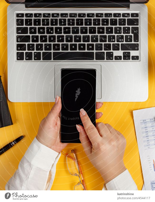 Business Frau Hände mit Smartphone Ansicht von oben verwenden Dokumente Handy-Berichte gelb Laptop Schreibtisch Büro Draufsicht Kaffee Kaukasier gesichtslos