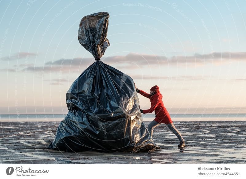 Eine Frau schiebt einen großen schwarzen Müllsack ans Ufer Ökologie Kunststoff Flaschen Sammlung Säuberung bedrohlich Verschmutzung recycelbar Umweltbedrohung