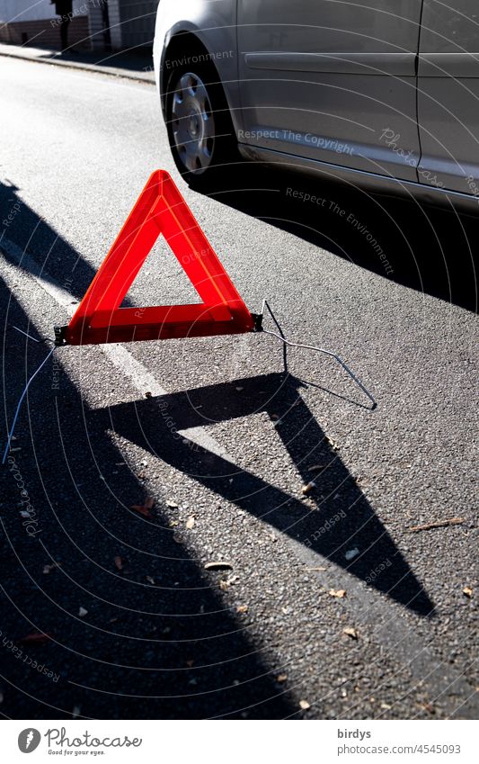 Leuchtend rotes Warndreieck mit Schattenwurf an einem Pannenfahrzeug, Unfallstelle. Auto leuchtend leuchtend rot Dreieck Warnung Gefahrenstelle Autopanne