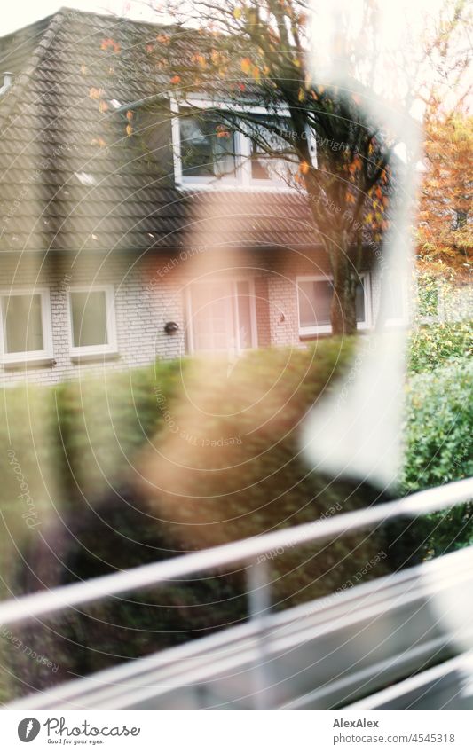 Unscharfe Silhouette einer Frau hinter einem Fenster, in dem sich das Nachbarhaus klar spiegelt junge Frau kurze Haare brünett schauen natürlich authentisch