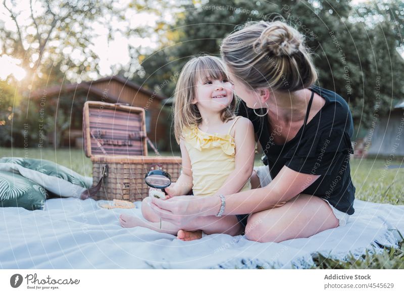 Glückliche Mutter und Tochter, die beim Picknick einen Käfer mit einer Lupe untersuchen Frau Kind Umarmung Insekt Zusammensein Interesse Natur Eltern jung blond