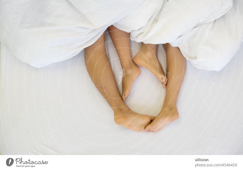 Nahaufnahme von vier Füßen, männlich und weiblich, auf dem Bett - Liebespaar beim Sex unter weißer Decke im Schlafzimmer - Konzept des sinnlichen und intimen Moments, Raum kopieren