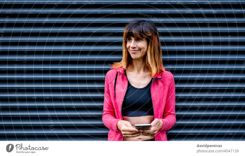 Sportlerin mit Mobiltelefon Lächeln Gitterrost-Hintergrund Mobile posierend Porträt Taille hoch Fitness Frau Smartphone Gesundheit Lifestyle sportlich Athlet