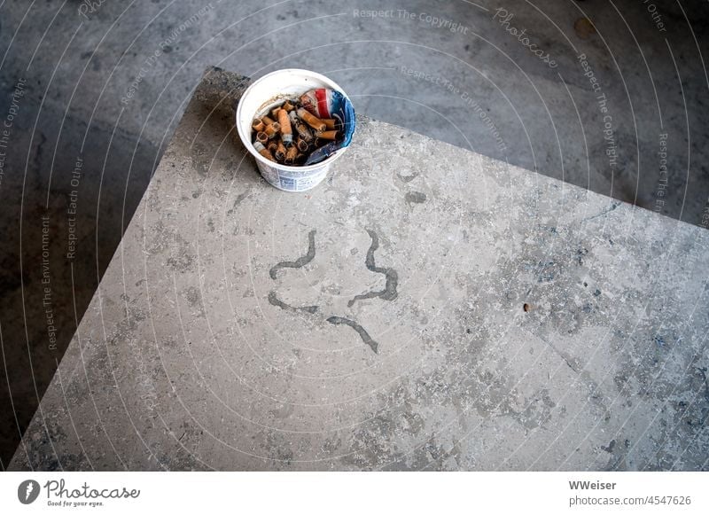 Die Handwerker haben nach der Arbeit einen ehemaligen Joghurtbecher voller Zigarettenstummel hinterlassen Tisch Steinplatte sachlich nüchtern minimalistisch