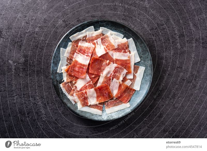 Spanischer Serrano-Schinken in Scheiben auf schwarzem Teller auf schwarzem Hintergrund Prosciutto Italienisch Aufschnitt Lebensmittel Schweinefleisch geheilt