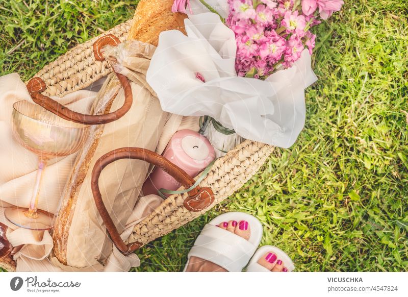 Picknickkorb mit Kerze, Blumen, Baguette und Champagnerglas auf grünem Gras Hintergrund mit Frau Füße. Romantische Sommer-Picknick Vorbereitung. Ansicht von oben.