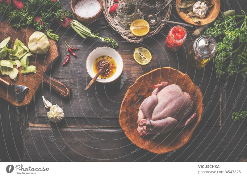 Rohes ganzes Huhn auf rustikalem Holztisch mit Marinade, Knoblauch, Apfel, Gewürzen, Gläsern und Küchenutensilien. Kochen Vorbereitung zu Hause mit rohem Fleisch und schmackhaften Zutaten. Ansicht von oben.
