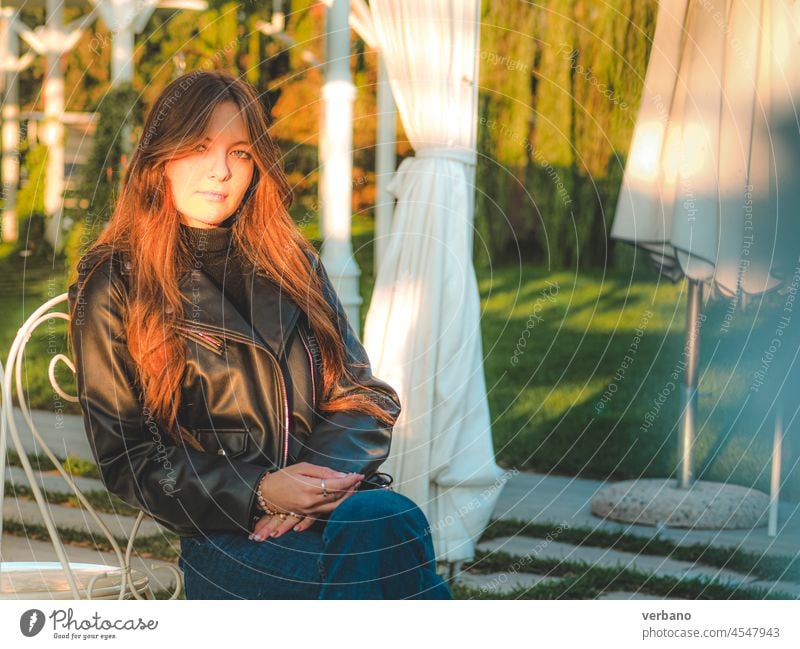 Mädchen in Blue Jeans und Lederjacke sitzt bei Sonnenuntergang im Freien Frau Mode lässig jung Jeanshose weiß schön Jacke attraktiv Jeansstoff Stil Kaukasier