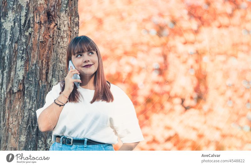 Junge Frau im Park einen Anruf mit dem Mobiltelefon auf schönen sonnigen Tag Herbst. Weißes Tshirt Kleidung leeren Raum. Redhead Schönheit Körper positiv Mädchen. Bunte Hintergrund Kopie Raum