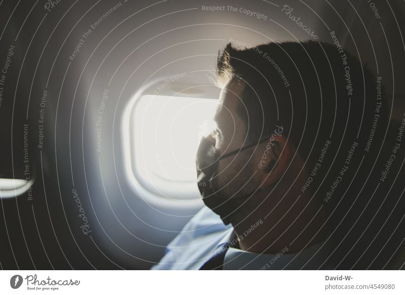 Mann mit Maske schaut aus dem Fenster eines Flugzeugs Pandemie Atemschutzmaske Maskenpflicht urlaub fliegen reisen Sehnsucht Schützen Tourist