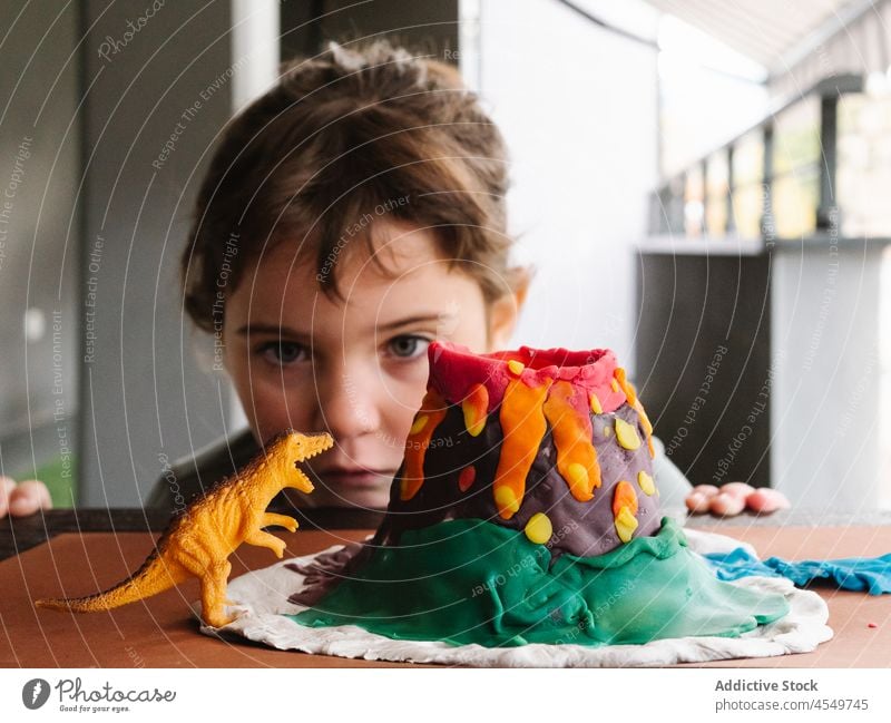 Kleines Mädchen spielt mit Spielzeugdinosaurier, nachdem es einen Vulkan aus Knetmasse geformt hat Kind spielen Dinosaurier wenig Figur Kindheit kreativ