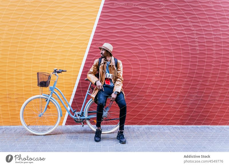 Schwarzer Mann auf Fahrrad in der Nähe der bunten Wand Straße Zeitvertreib Radfahrer Hobby Freizeit Laufsteg Streetstyle Kleidungsstück anhaben Vorschein