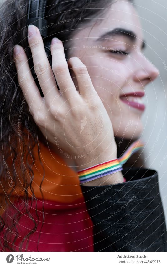 Fröhliche hispanische Lesbe mit LGBT-Armband beim Musikhören lgbt Frau Kopfhörer zuhören Straße Homosexualität gleich unkonventionell lesbisch meloman