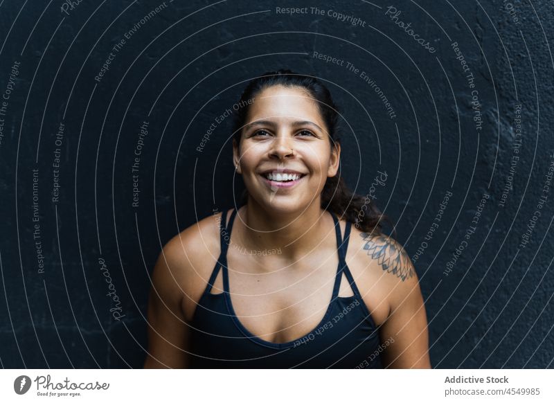 Hispanische Sportlerin an der Wand stehend Frau sportlich Sportkleidung Training Gesunder Lebensstil Wellness Lächeln Fitness muskulös Glück Straße froh
