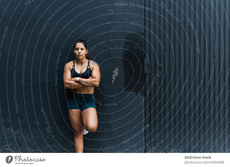 Hispanische Sportlerin an der Wand stehend Frau sportlich Sportkleidung Training Gesunder Lebensstil Wellness Fitness muskulös Straße Dame die Arme verschränkt