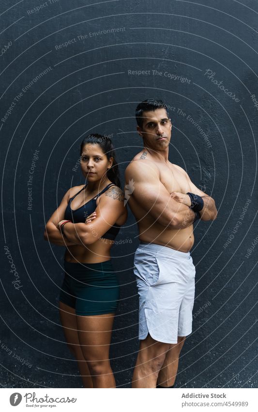 Seriöses hispanisches sportliches Paar in der Nähe der Mauer Sportler Training Wand Gesunder Lebensstil Wellness Fitness muskulös die Arme verschränkt