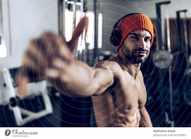 Ethnischer Sportler zeigt beim Training die Geste des lockeren Hängens Mann Athlet ohne Hemd Shaka Kopfhörer gestikulieren stark muskulös Fitnessstudio männlich