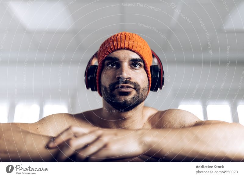 Mann ohne Hemd stellt Kopfhörer vor dem Training mit der Langhantel ein Athlet muskulös Bauchmuskeln stark Curl-Hantel zuhören männlich Sportler nackter Torso
