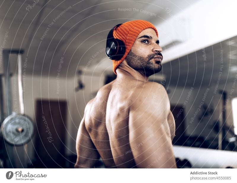 Muskulöser Sportler mit Hut und Kopfhörern im Fitnessstudio Mann Athlet muskulös Training Musik zuhören Drahtlos ohne Hemd männlich Muskel Kraft Wellness