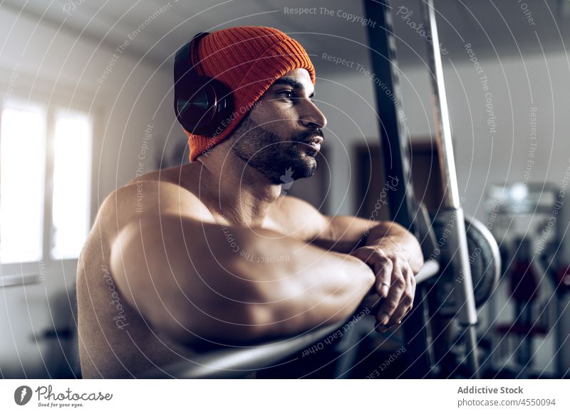 Mann ohne Hemd stellt Kopfhörer vor dem Training mit der Langhantel ein Athlet muskulös Bauchmuskeln stark Curl-Hantel zuhören männlich Sportler nackter Torso