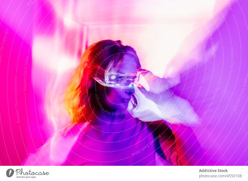 Junge Frau mit Led-Brille Augen im Studio Videospiel kreativ futuristisch Virtuelle Realität Metaversum neonfarbig Langzeitbelichtung Licht farbenfroh leuchten