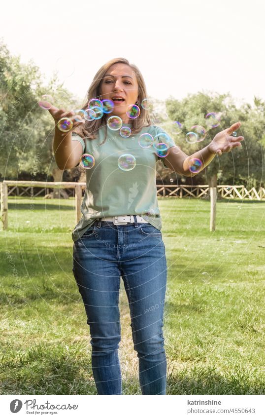 Frauen spielen mit Seifenblasen in einem Park Erwachsener mittleres Alter Spielen T-Shirt Lächeln Zauberei u. Magie lässig Glück Spaß grün Gras Attrappe