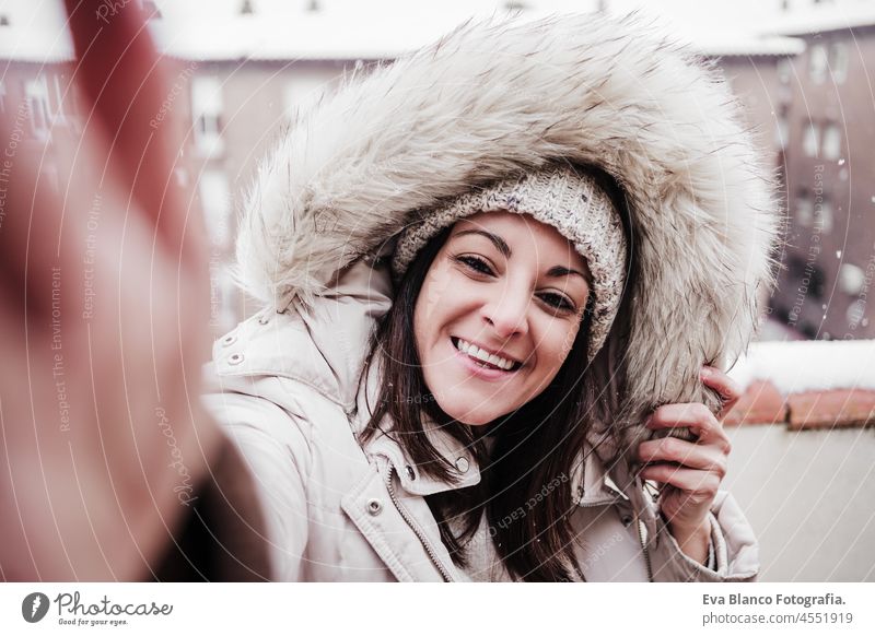 glückliche Frau auf der Terrasse zu Hause genießen Schnee während der Aufnahme von Selfie mit Handy, Nachbarschaft Hintergrund. Schnee in der Stadt Großstadt