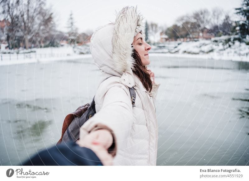 glückliche kaukasische Frau, die die Hand ihres Freundes hält, vor einem zugefrorenen See in der Wintersaison stehend. Liebe und Lebensstil im Freien
