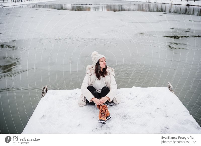 glückliche Frau mit geschlossenen Augen sitzt auf Pier vor gefrorenen See in der Stadt. Reisen und Lifestyle im Winter in der Stadt Schnee Landschaft