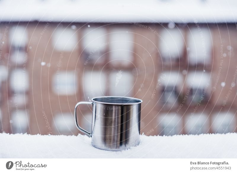 Metallische Tasse heißes Getränk, Tee oder Kaffee, auf der Terrasse bei Schnee im Winter, Nachbarschaft Hintergrund. Schnee in der Stadt. Niemand trinken