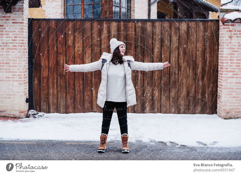 Backpacker Frau zu Fuß in der Stadt im Winter bei Schneefall. Glückliche Frau mit ausgestreckten Armen genießt im Freien laufen Großstadt kalt Spielen Park
