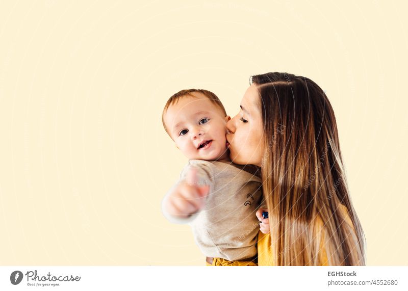 Porträt einer jungen Geschäftsfrau, die ihren kleinen Jungen vor gelbem Hintergrund küsst Mama Arbeit Kuss Baby Familie befähigen beschäftigt Mutter Büro