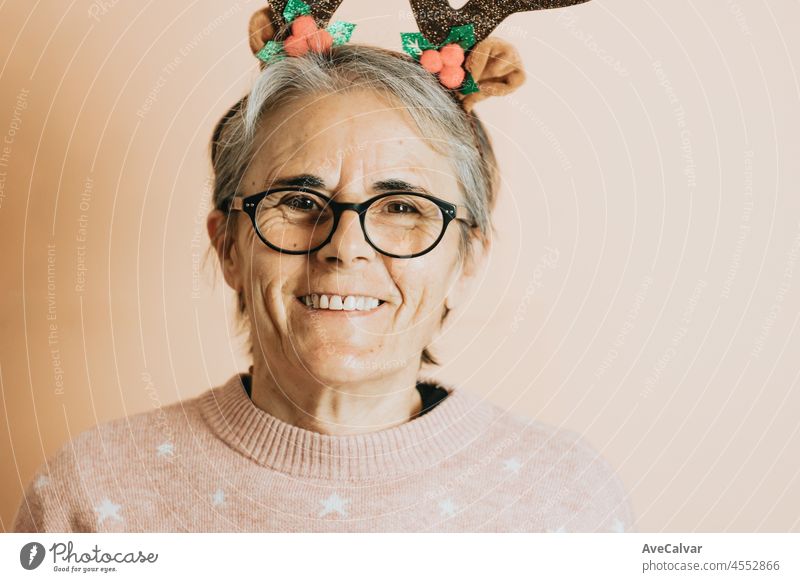 Happy Joyful Senior alten weißen Haaren Frau trägt Rentier Hörner Hut lächelnd beim Spielen und Spaß haben. steht gegen eine Farbe Hintergrund. Wearing Weihnachten Kleidung. Kopierfläche. Werbefläche