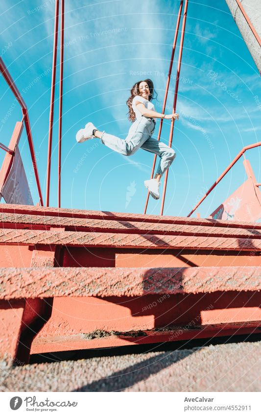 Urban Bild einer jungen Frau mit langen Haaren springen in den Himmel, Weitwinkelaufnahme. Modernes Outfit weißes Hemd blaue Jeans weiße Schuhe. Stadtleben Stil. Freiheit und Freiheit Konzept