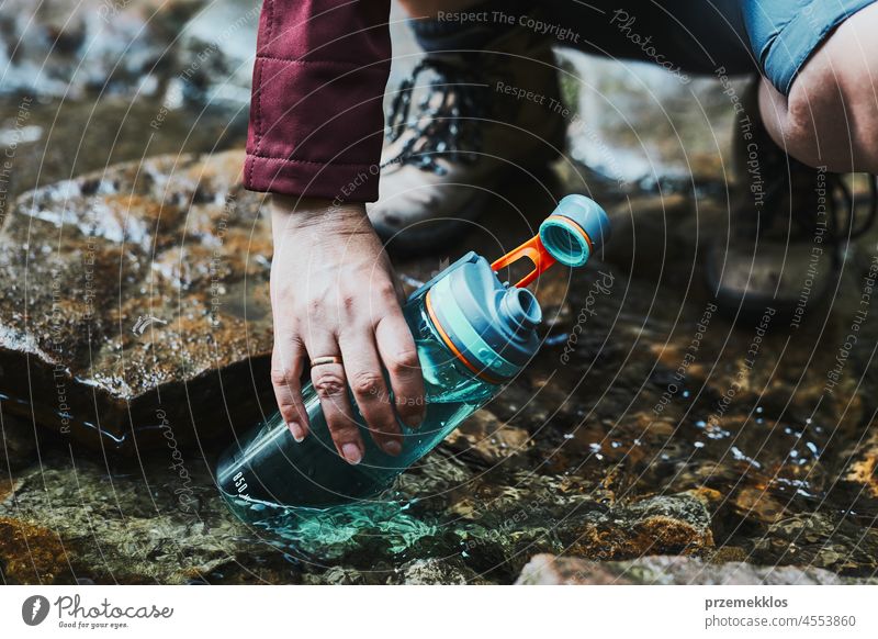 Frau, die beim Trekking in den Bergen reines Wasser aus einem Bergbach in eine Flasche füllt Abenteuer Ausflug reisen wandern durstig strömen Urlaub Reise